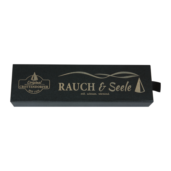 Eine rechteckige, schwarze Schubbox „RAUCH & Seele“ von Original Crottendorfer Räucherkerzen, verziert mit goldener Schrift und minimalistischen Grafiken. Auf der Schachtel stehen die Aufschriften „still, achtsam, wärmend“ – damit ist sie ein ideales Geschenkset für Liebhaber feiner Räucherutensilien.