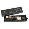 Eine schicke schwarze „Schubbox RAUCH & Seele“ von Original Crottendorfer Räucherkerzen enthält eine sorgfältig zusammengestellte Auswahl an Räucherzubehör, darunter Räucherkegel, einen Glashalter, eine Holzfigur, Streichhölzer, einen Metallhalter und eine Packung mit der Aufschrift „St. Felix“ – alles wunderschön arrangiert in einer eleganten Geschenkbox vor weißem Hintergrund.
