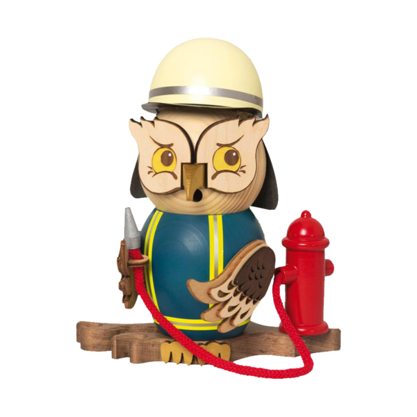 Die Rauchfigur Eule Feuerwehr von Drechslerei Kuhnert ist eine skurrile Eulenfigur, die als Feuerwehrmann verkleidet ist, mit gelbem Helm und blauem Outfit mit gelben Streifen. Sie hält einen Schlauch, der an einen roten Hydranten angeschlossen ist, und steht stolz auf einem Holzsockel.