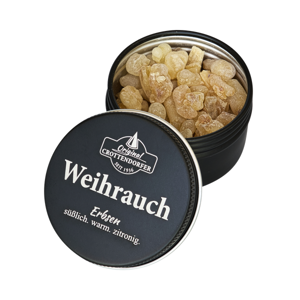 Eine runde schwarze Blechdose mit der Aufschrift „Weihrauch in der Schraubdeckeldose“ von Original Crottendorfer Räucherkerzen enthält hellbraune, unregelmäßig geformte Bonbons. Der teilweise geöffnete Deckel gibt den Blick auf Bonbons frei, die ein süßes, warmes Zitronenaroma verströmen – ideal für die Meditation.
