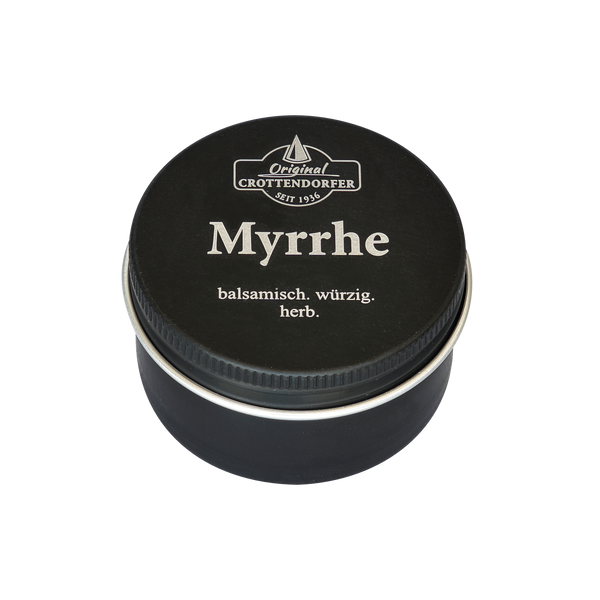 Eine kleine schwarze Blechdose mit der Aufschrift „Myrrhe in der Schraubdeckeldose“ von Original Crottendorfer Räucherkerzen, auf deren Deckel die Worte „balsamisch. würzig. herb.“ zu lesen sind, ist vor einem weißen Hintergrund fotografiert.