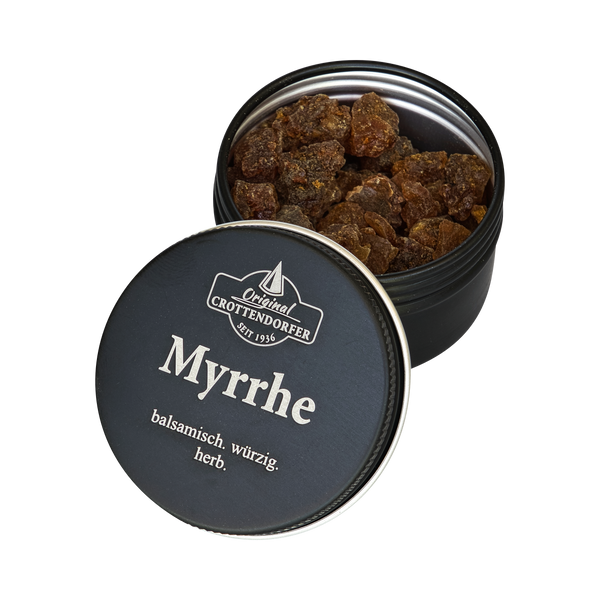 Eine runde schwarze Blechdose mit der Aufschrift „Myrrhe in der Schraubdeckeldose“ von Original Crottendorfer Räucherkerzen enthält braune Harzstücke. Auf dem teilweise geöffneten Deckel sind ein deutscher Text und das Markenlogo auf weißem Hintergrund zu sehen.