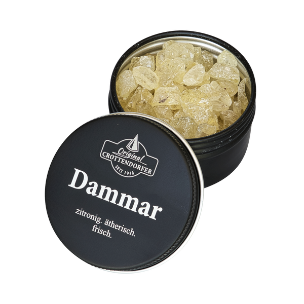 Eine schwarze Blechdose mit der Aufschrift „Dammar in der Schraubdeckeldose“ von Original Crottendorfer Räucherkerzen steht mit halb geöffnetem Deckel da und gibt den Blick auf hellgelbe Harzkristalle frei, die einen frischen, zitronigen und stimmungsaufhellenden Duft versprechen.