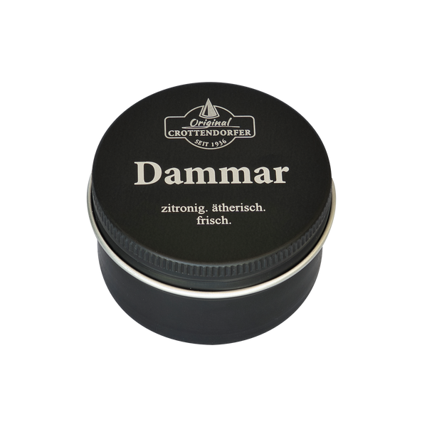 Auf einer schwarzen Blechdose mit der Aufschrift „Dammar in der Schraubdeckeldose“ von Original Crottendorfer Räucherkerzen ist in weißer Schrift der Text „zitronig. ätherisch. frisch.“ zu lesen, wodurch der stimmungsaufhellende, ätherische Duft vor dem weißen Hintergrund besonders hervorgehoben wird.