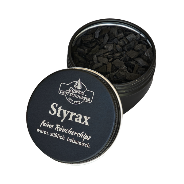 Eine runde schwarze Dose mit der Aufschrift „Styrax Räucherchips in der Schraubdeckeldose“ von Original Crottendorfer Räucherkerzen steht mit halb geöffnetem Deckel da, sodass man die schwarzen Chips im Inneren sehen kann. Der warme, süße, balsamische Duft ist perfekt für Fans von Räucherwerk.