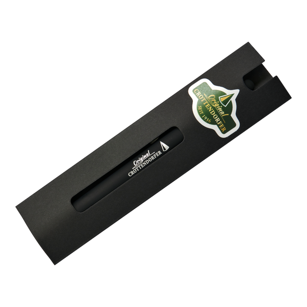 Ein Kugelschreiber Original Crottendorfer mit Touchpen, schwarz, in einer schwarzen Schachtel mit Ausschnitt und einem grünen Bergaufkleber auf der rechten Seite. Weißer Hintergrund.