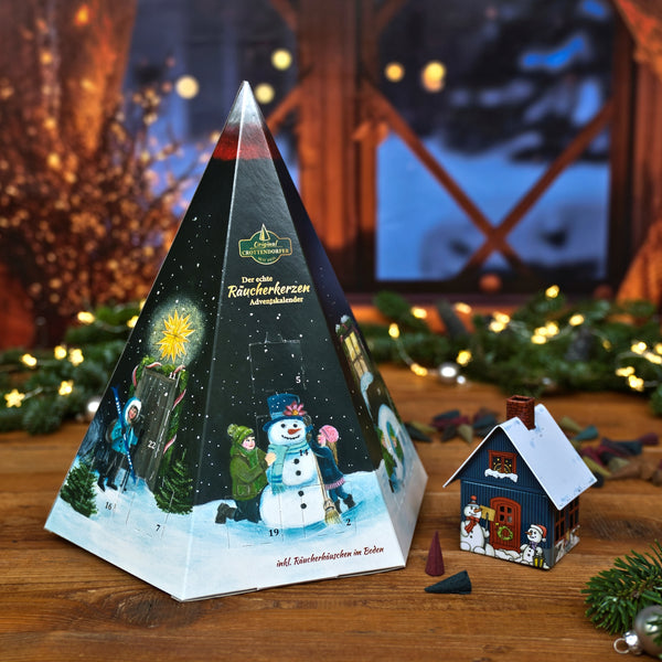 Original Crottendorfer Räucherkerzen – Räucherkerzen-Adventskalender: Pyramide in Form einer Pyramide mit Wintermotiven, präsentiert neben einem hausförmigen Räuchergefäß.