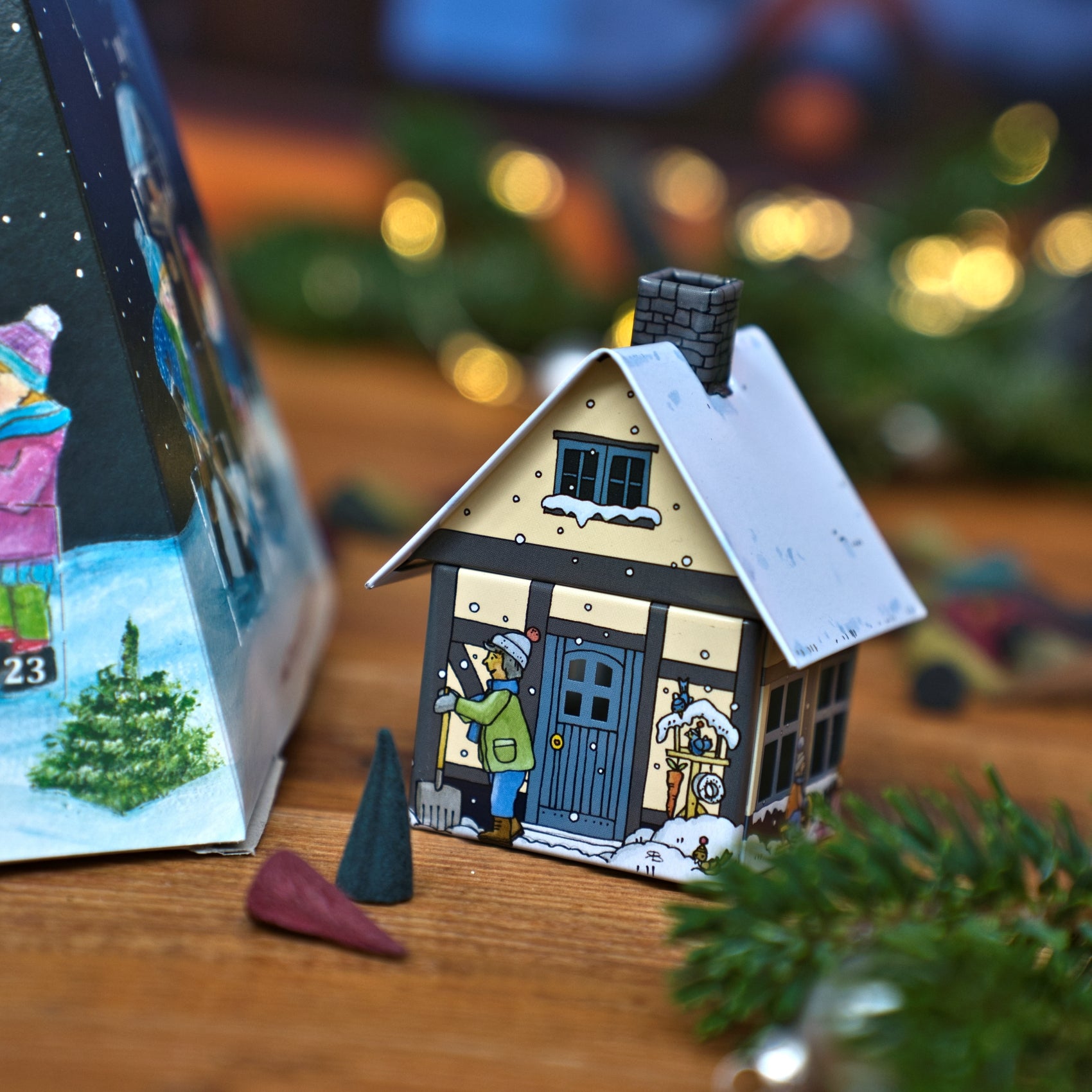 Ein kleiner, hausförmiger Räuchergefäß neben einem Original Crottendorfer Räucherkerzen-Adventskalender – Pyramide und zwei Räucherkerzen auf einer Holzunterlage.