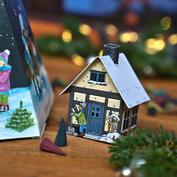 Ein kleiner, hausförmiger Räuchergefäß neben einem Original Crottendorfer Räucherkerzen-Adventskalender – Pyramide und zwei Räucherkerzen auf einer Holzunterlage.