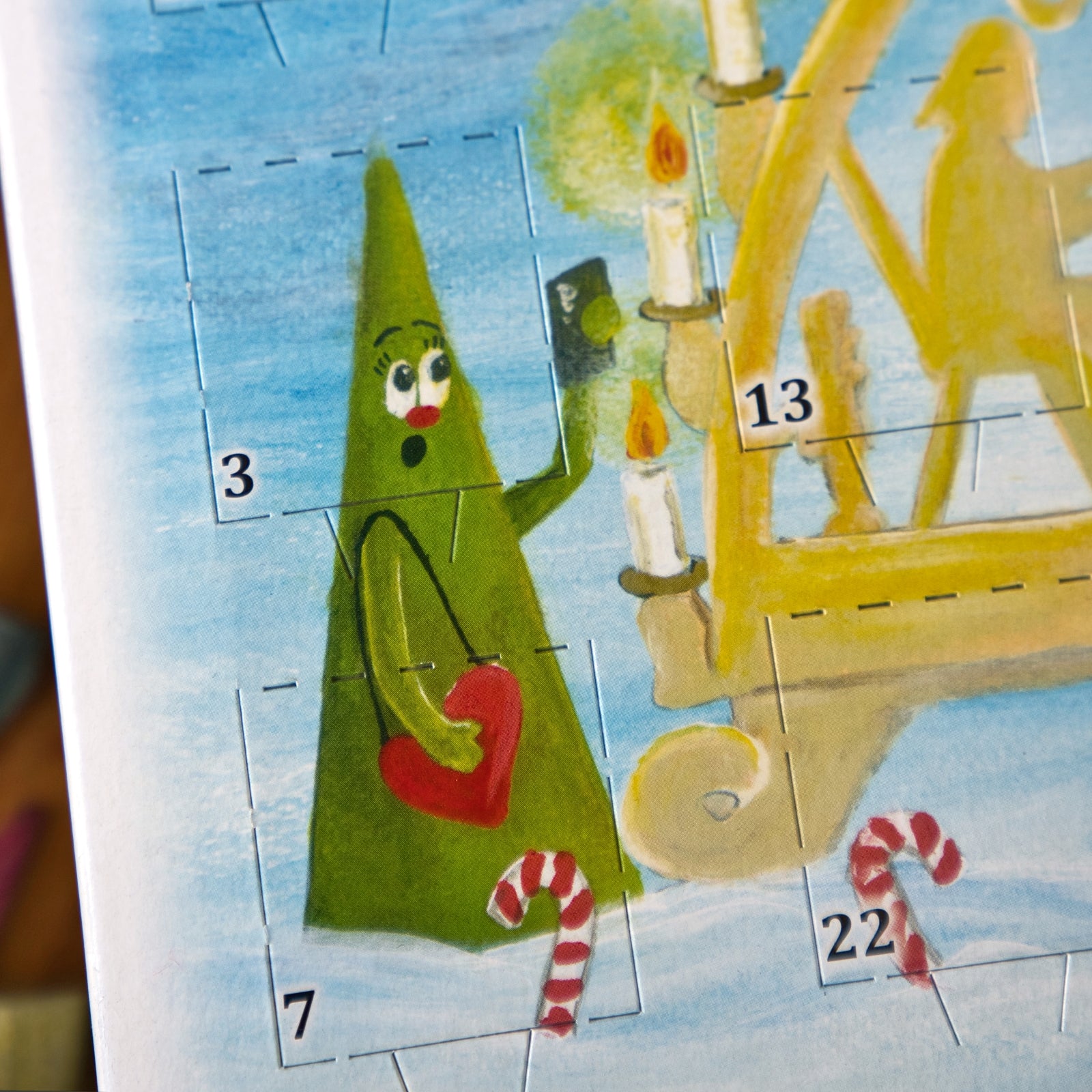 Vor einem blauen Hintergrund steht ein fröhlicher, im Cartoon-Stil gestalteter grüner, dreieckiger Baum, der ein rotes Herz in den Händen hält, neben einem goldenen Kerzenleuchter mit brennenden Kerzen. Zu sehen sind die nummerierten Türchen des „Räucherkerzen-Adventskalenders 2026 – Querformat“ von Original Crottendorfer Räucherkerzen, die den erzgebirgischen Weihnachtszauber unterstreichen.