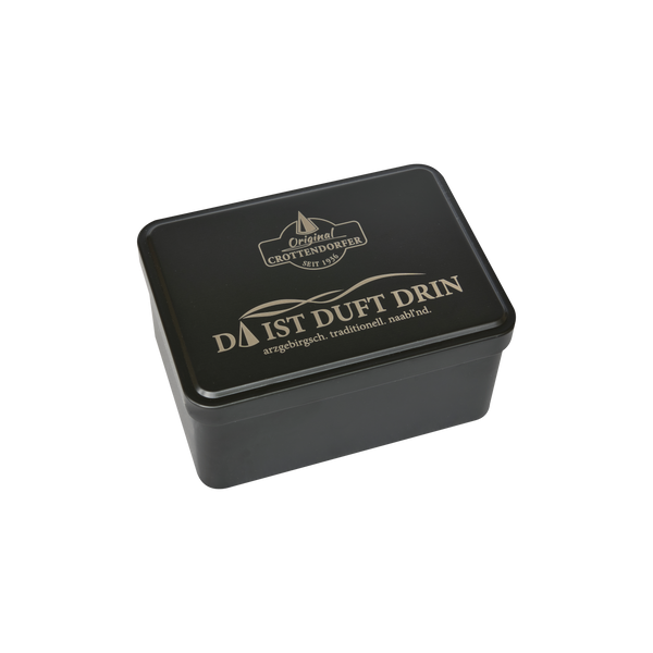 Eine rechteckige schwarze Aufbewahrungsbox von Original Crottendorfer im Stil einer Blechdose mit Scharnierdeckel, auf deren Deckel der goldene deutsche Schriftzug „DA IST DUFT DRIN“ sowie das Markenlogo zu sehen sind, fotografiert vor weißem Hintergrund.