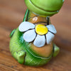 Eine Nahaufnahme des KU Räucherdrache mit Blume von Kurilin DECO, einer handgefertigten grünen Keramikdrachenfigur mit einer weiß-gelben Blume um den Hals, die auf einer Holzfläche sitzt.