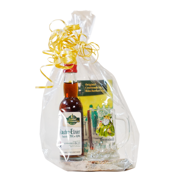 Das Geschenkset Grenzwald von Original Crottendorfer kommt in transparenter Zellophanverpackung mit gelber Schleife und enthält ein Mini-Räucher-Elixier Kräuter, ein Schnapsglas mit Figurenillustrationen .