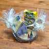Ein in Klarsichtfolie verpackter Geschenkkorb mit weißen Bändern präsentiert das „Geschenkset Räucherhäuschen + Räucherkerzen“ von Original Crottendorfer Räucherkerzen mit Musterhaus, Gewürzflasche und Kühne-Artikel elegant arrangiert auf Holz.