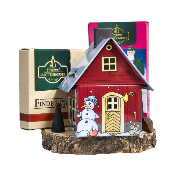 Das Geschenkset Räucherhäuschen Wintermotiv mit Räucherkerzen und Memo-Spiel von Original Crottendorfer Räucherkerzen zeigt ein bezauberndes rotes Räucherhäuschen mit Schneemann, ausgestellt auf Holz vor zwei Geschenkboxen, sowie einen Räucherkegel und eine Katzenillustration.