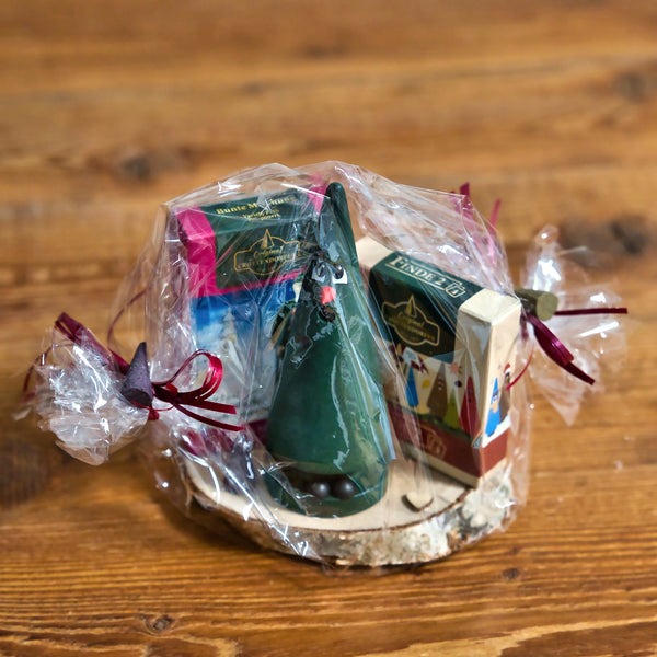Das Geschenkset Tina Tanne mit Räucherkerzen und Memo-Spiel von Original Crottendorfer Räucherkerzen ist in klarem Kunststoff mit kastanienbraunen Bändern verpackt, mit grünem Baumschmuck und bunten Schachteln, alles auf einer Holzoberfläche.