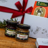 Zwei Gläser mit Brombeer-Thymian und Bratapfel-Fruchtaufstrich stehen auf einer Holzplatte vor einer festlichen, geschnürten weihnachtlichen Geschenkdose, die sich ideal mit dem Original Crottendorfer Stollen Geschenkset kombinieren lässt.