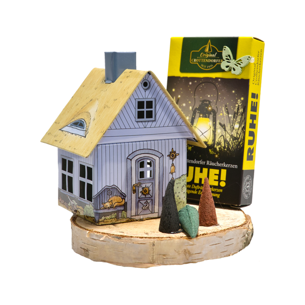 Das „Geschenkset Räucherhäuschen + Räucherkerzen“ von Original Crottendorfer Räucherkerzen besteht aus einem Räucherhäuschen mit Holzdach auf einem Sockel, vier duftenden Räucherkerzen davor und einer Schachtel mit Laternenmotiv mit der Aufschrift RUHE!, die eine bezaubernde Präsentation ergibt.