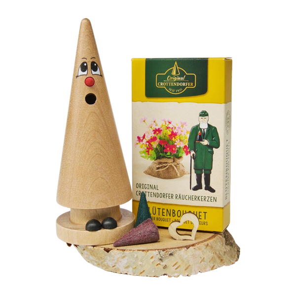 Das Geschenkset „Ziegenbein + Räucherkerzen“ von Original Crottendorfer Räucherkerzen besteht aus einem hölzernen Räuchergefäß mit einem Gesicht auf einem Holzsockel sowie einer gelben Schachtel mit Räucherkegeln – auf weißem Hintergrund präsentiert, eignet es sich perfekt als Ostergeschenkset.