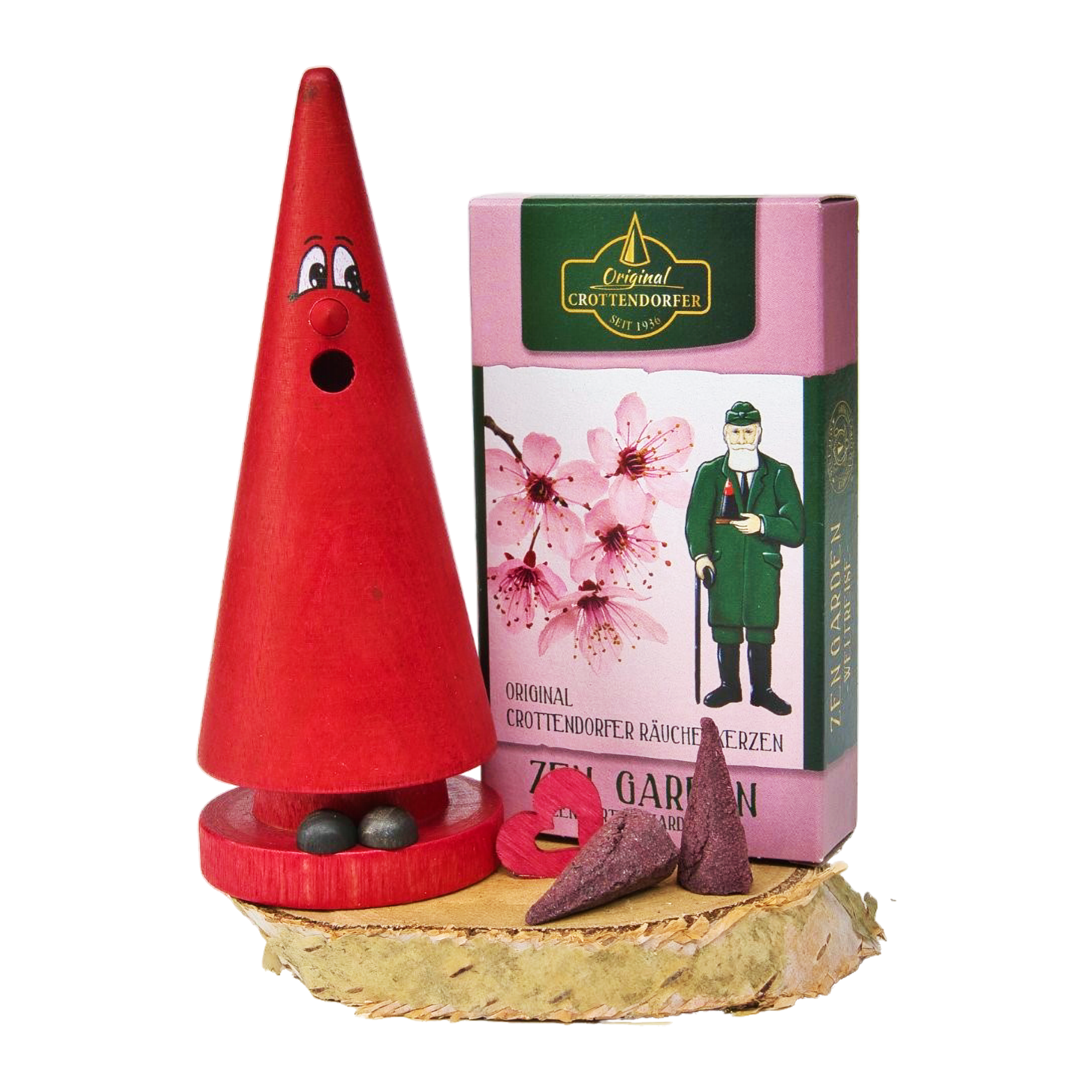 Ein roter, kegelförmiger Räucherkerzenhalter mit Augen und Mund steht auf einem Holzsockel neben Original Crottendorfer Räucherkerzen, einem herzförmigen Stück und einer rosa Blumenbox aus dem Geschenkset „Ziegenbein + Räucherkerzen“.