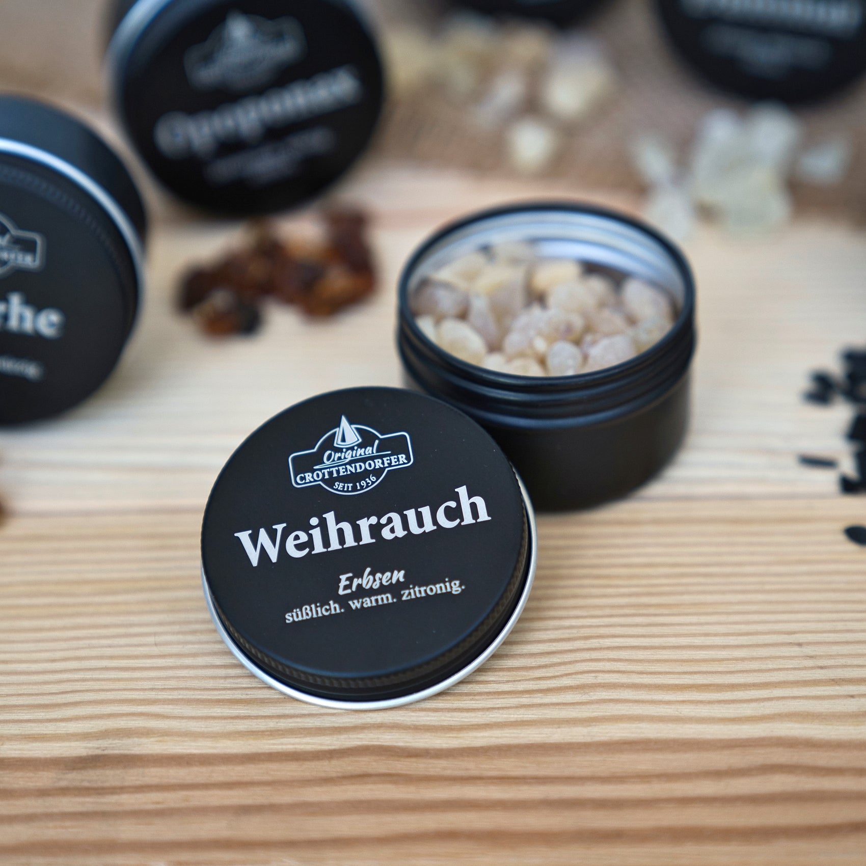 Eine offene schwarze Dose mit der Aufschrift „Weihrauch in der Schraubdeckeldose“ von Original Crottendorfer Räucherkerzen gibt den Blick auf helles Harz im Inneren frei, das sich ideal zur Meditation eignet. Im Hintergrund stehen weitere, unscharf abgebildete Räucherwerk-Dosen und Harze auf einer Holzunterlage.