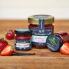Drei Gläser „Original Crottendorfer Hausgemachter Fruchtaufstrich“ (200 g) sind auf einer Holzunterlage zu sehen, umgeben von frischen Erdbeeren und einer Vanilleschote. Die deutschen Etiketten weisen darauf hin, dass dieser Fruchtaufstrich hausgemacht und vegan ist.
