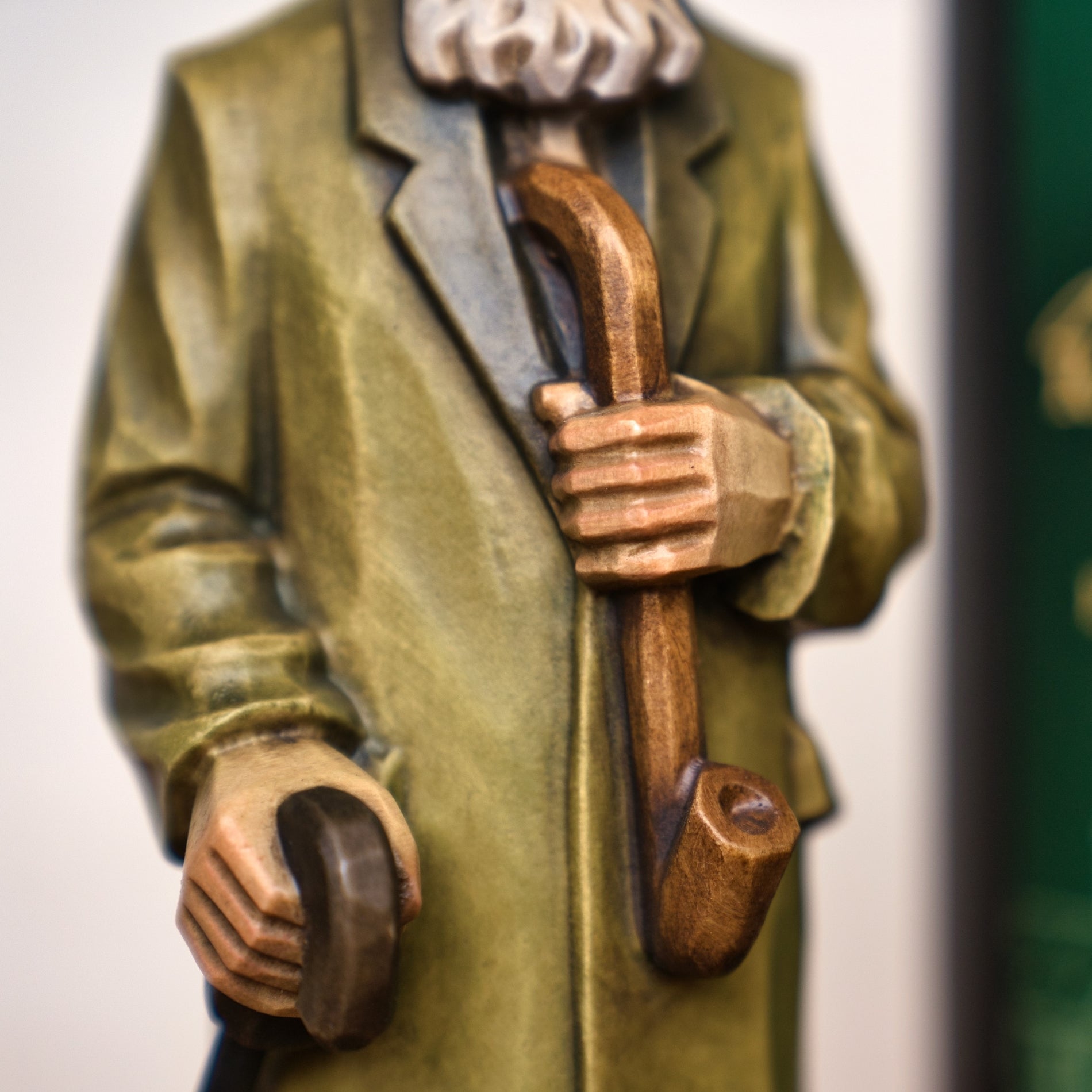 Nahaufnahme des Jubiläums Räuchermann in der schwarzen Geschenkdose von Original Crottendorfer Räucherkerzen, dargestellt im grünen Mantel mit Stock und Pfeife - ein schönes Stück erzgebirgischer Handwerkskunst. Gesicht nicht sichtbar.