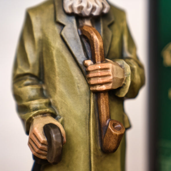 Nahaufnahme des Jubiläums Räuchermann in der schwarzen Geschenkdose von Original Crottendorfer Räucherkerzen, dargestellt im grünen Mantel mit Stock und Pfeife - ein schönes Stück erzgebirgischer Handwerkskunst. Gesicht nicht sichtbar.