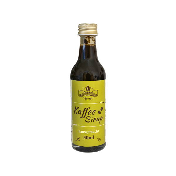 Der Original Crottendorfer Hausgemachter Kaffeesirup ist in einer 50-ml-Glasflasche mit gelbem Etikett mit den Aufschriften „Kaffeesirup“ und „hausgemacht“ erhältlich und eignet sich ideal für Eiskaffee oder Cocktails. Die dunkle Flüssigkeit ist mit einem Schraubverschluss auf schwarzem Hintergrund verschlossen.