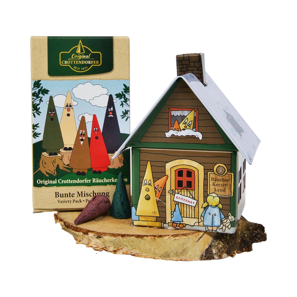 Das Geschenkset „Räucherhäuschen + Räucherkerzen“ von Original Crottendorfer Räucherkerzen enthält einen dekorativen Räucherhalter mit Comicfiguren auf einem Holzsockel, bunte Kegelräucherstäbchen sowie eine Schachtel mit der Aufschrift „Bunte Mischung“ – ein ideales Geschenkset.