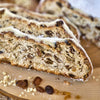 Drei Scheiben Original Crottendorfer Raacherkerzl-Christstollen mit Rosinen, dicht mit sichtbaren Trockenfrüchten und Nüssen bestückt, liegen auf einer Holzunterlage mit gestreuten Rosinen und gehackten Nüssen und erinnern an klassisches Stollen-Weihnachtsgebäck.