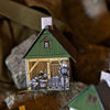Ein kleines Papiermodell, das Räucherhäuschen „Huthaus“ von Original Crottendorfer Räucherkerzen, steht zwischen Felsen und zeigt auf der Vorderseite illustrierte Bergleute – einer schiebt eine Karre, ein anderer lehnt neben Holzbalken. Es ist als Räucherkerzenhalter konzipiert und besticht durch eine grüne Fassade, einen Schornstein mit Steinmuster sowie realistische Metalldetails.