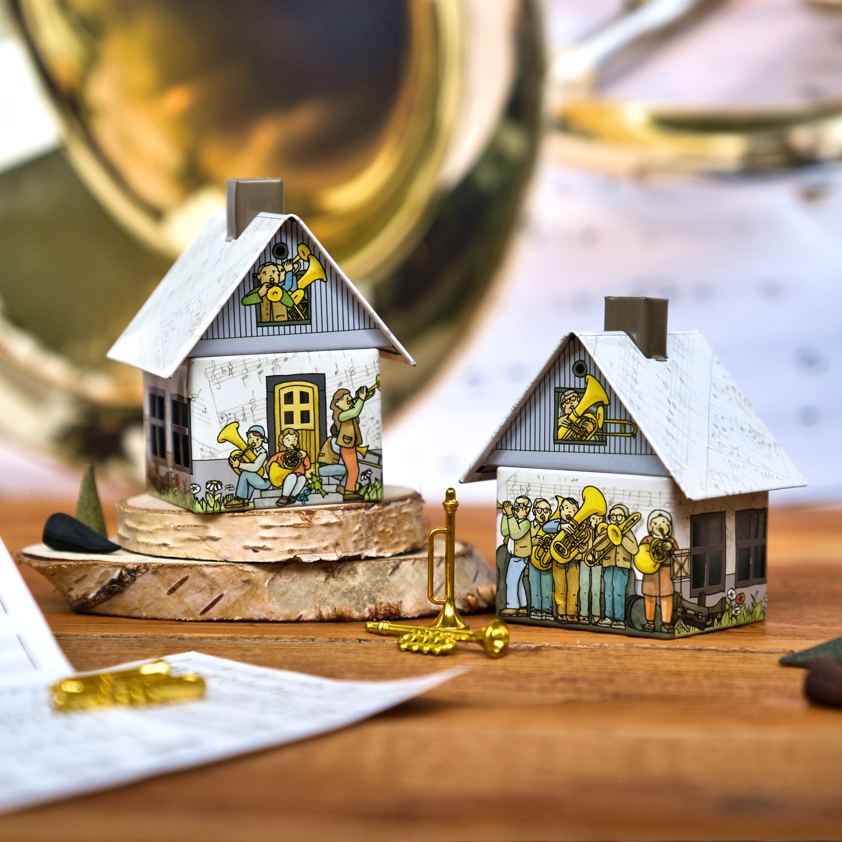 Das Räucherhäuschen Posaunenchor von Original Crottendorfer Räucherkerzen besteht aus zwei kleinen Papierhäuschen, die mit Musikern aus Messing geschmückt sind. Sie stehen auf Birkenrindenholz und sind mit Metalltrompeten und musikalischen Accessoires bestückt.