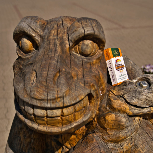 Eine Nahaufnahme einer großen Froschskulptur aus Holz von „Original Crottendorfer Räucherkerzen“ für die Deutsche Speedcarving-Meisterschaft 2026. In ihrer Wange steckt ein Ticket mit der Aufschrift „Finale“, rechts ist teilweise eine kleinere Froschskulptur zu sehen.