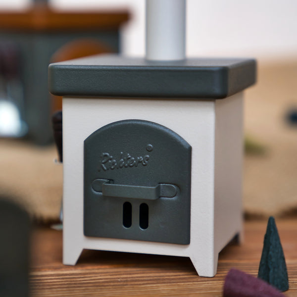 Ein kompakter, quadratischer, grau-weißer Hartmut Richter Räucherofen Hüttenofen aus Metall mit einer Fronttür mit der Aufschrift "Räder" und einem integrierten Aschekasten, dargestellt auf einer Holzfläche mit unscharfem Hintergrund.