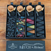 Vier „RAUCH & Heimat“-Sets von Original Crottendorfer Räucherkerzen, die jeweils kleine Holzschälchen, schwarze Metallschaufeln sowie bunte Räucherkegel und -stäbchen enthalten, sind ordentlich auf einer Holzunterlage angeordnet. Auf dem Deckel der Schachtel prangt der Schriftzug „Rauch & Heimat“, was diese Geschenksets zum perfekten Geschenk für Liebhaber hochwertiger Räucheraccessoires macht.