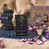 Auf einer dunklen Fläche steht eine schwarze Schachtel mit der Aufschrift „Räucherkerzen Wild Romance“ von Original Crottendorfer Räucherkerzen, umgeben von Räucherkegeln, Gläsern, getrockneten Blütenblättern und gestapelten Räucherkisten vor einem Hintergrund aus Sackleinen. Die Szene weckt den Duft des Mittelmeerraums, wobei sich Noten von frischen Feigen und zarte Akzente von Weihrauch in der Luft vermischen.