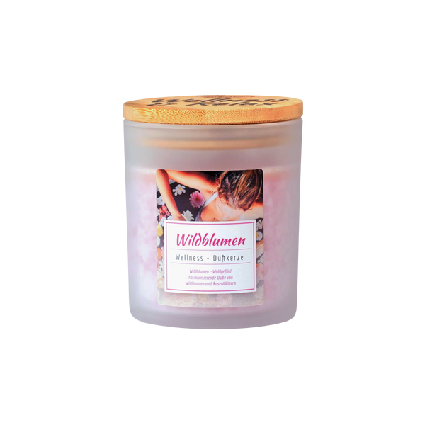 Die Candle Factory Wellness-Duftkerze Wildblumen ist eine Kerze in einem Milchglas mit Holzdeckel. Das Etikett zeigt eine Frau inmitten von Blumen und einen deutschen Text über Stearin, Wellness-Duftkerzen und von der Natur inspirierte Düfte.