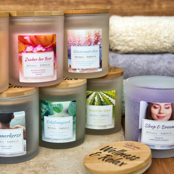Das Aromabadekissen "Wintermärchen" von Candle Factory präsentiert sich in einem Milchglas mit einem Holzdeckel mit der Aufschrift Wellness & Relax, der an einen winterlichen Wellness-Duft erinnert. Aufgerollte Handtücher tragen zur entspannenden Präsentation bei.