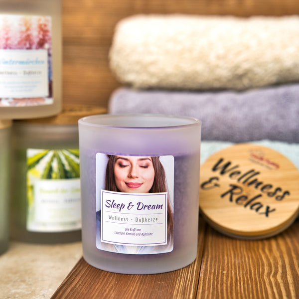 Das Aromabadekissen "Sleep & Dream" von Original Crottendorfer ruht auf einer Holzfläche neben gefalteten Handtüchern und lädt mit seinem beruhigenden Duft zum Entspannen ein. Auf der Verpackung ist eine ruhige Frau mit geschlossenen Augen abgebildet und die Aufschrift Wellness & Relax zu lesen.