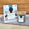Eine Dose Candle Factory Aromabadekissen "Männerbad" mit Sandelholz Duft und eine Wellness & Relax Männerkerze sitzen auf einem grauen Handtuch vor einem Holzhintergrund. Beide zeigen auf ihren Verpackungen einen Mann, der ein entspannendes Bad genießt.