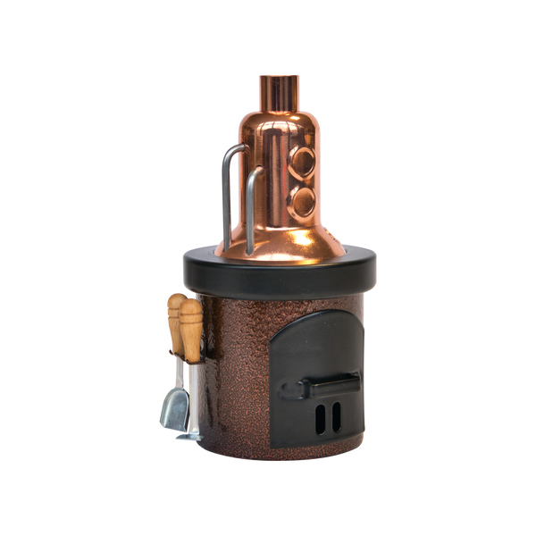 Der Räucherofen-Destillator von Hartmut Richter ist ein kompaktes Destillationsgerät aus Metall mit einer glänzenden Kupferplatte, einem schwarzen Aschekastenboden und Holzgriffen an der Seite, die vor einem schlichten weißen Hintergrund gezeigt werden.