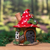 Eine kleine, verspielte Pilzhaus-Figur – das limitierte Räucherhaus „Eichelhaus“ aus Keramik von Original Crottendorfer – mit rotem, gepunktetem Dach, winzigen Fenstern, einer grauen Tür und Blattverzierungen ist auf einem hölzernen Messingteller vor einem verschwommenen Waldhintergrund ausgestellt.