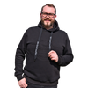 Vor rotem Hintergrund steht ein selbstbewusst lächelnder Mann, der einen Original Crottendorfer Kapuzenpullover mit Crottendorfer Räucherkerzen trägt und durch seine stylische Brille einen exklusiven Streetwear-Look besticht.