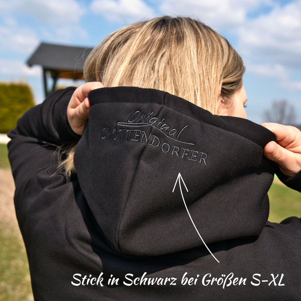 Draußen hebt eine Person in einem schwarzen Kapuzenpullover mit Crottendorfer Räucherkerzen (Original Crottendorfer) die Kapuze hoch und zeigt den gestickten Schriftzug „Original Crottendorfer“. Ein Pfeil und deutscher Text heben den exklusiven Hoodie in S-XL hervor.