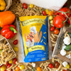 Eine Packung Miriquidi Sauerteig Pasta - Buchweizen liegt auf einem Tisch mit buntem Gemüse wie Tomaten, Paprika und Knoblauch, während spiralförmige vegane Sauerteig-Pasta sie für bessere Verträglichkeit umgibt.