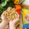 Hände, die einen Haufen ungekochter veganer Nudeln über einem Tisch mit frischem Paprika und Salat halten, daneben eine Packung Miriquidi Sauerteig Pasta - Buchweizen von Miriquidi Sauerteig Pasta für bessere Verdaulichkeit.