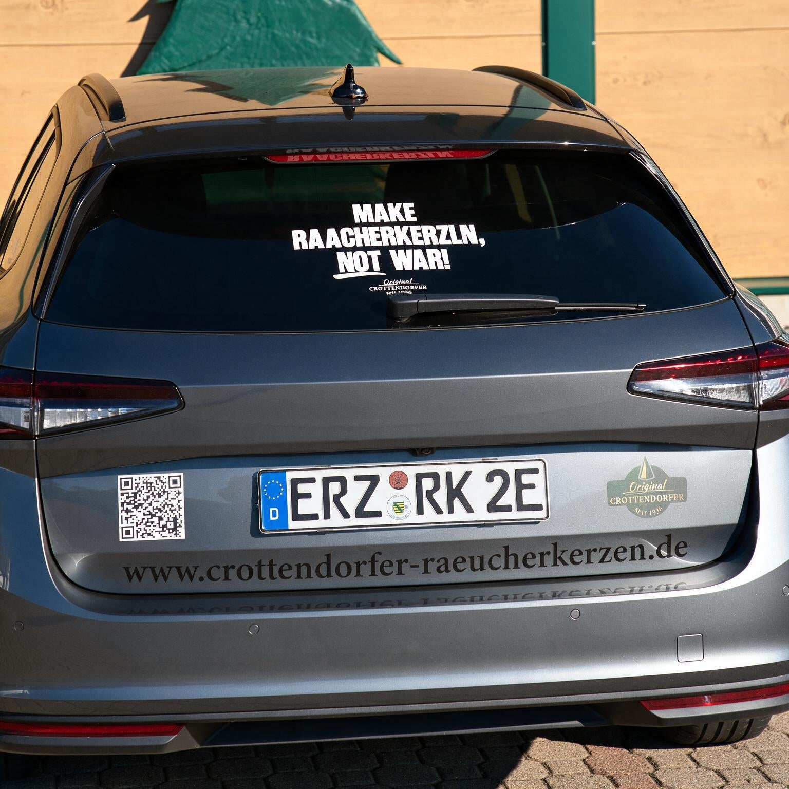 Ein silbernes Auto mit einem originalen Crottendorfer Heckscheibenaufkleber, auf dem „Make Raacherkerzln, not war!“ steht. Das Kennzeichen lautet ERZ RK 2E, und auf der Stoßstange ist eine Website aufgedruckt – ein Hinweis auf die Erzgebirgstradition und die beliebten Räucherkerzen.