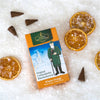 Die Packung Original Crottendorfer Räucherkerzen Winter-Orange liegt auf Schnee mit getrockneten Orangenscheiben und Zapfen drumherum. Die Verpackung zeigt eine Winterlandschaft mit einer warm gekleideten Figur, die ein zitrusartiges Aroma verströmt, das an frische Orangenblüten im Winter erinnert.