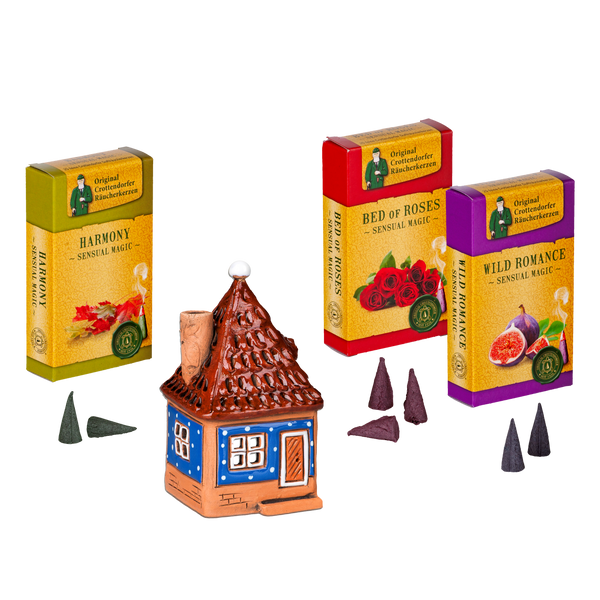 Drei farbenfrohe Original-Crottendorfer-Räucherstäbchenpackungen und ein Räucherhaus aus Keramik stehen auf weißem Hintergrund mit kegelförmigen Räucherstäbchen – Räucherhaus aus Keramik inkl. 3 Packungen Räucherstäbchen, ideal für festliche Weihnachtsdekoration.